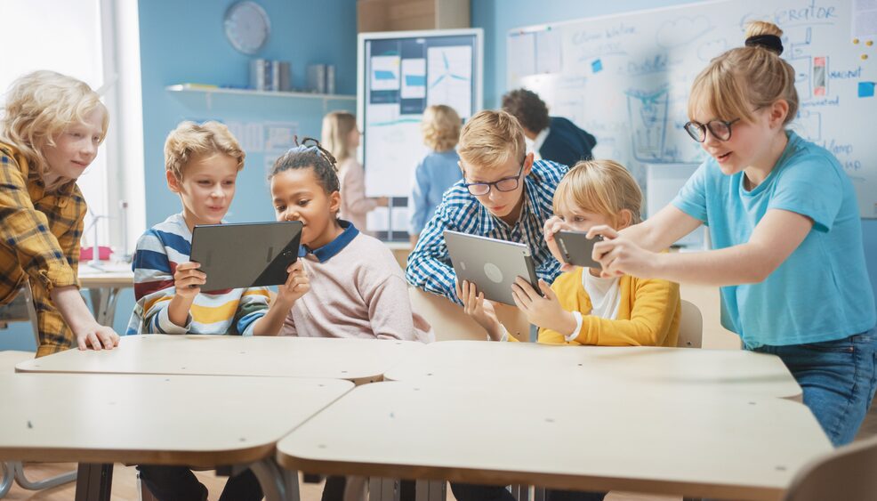 A group of children sitting at tables with ipads.