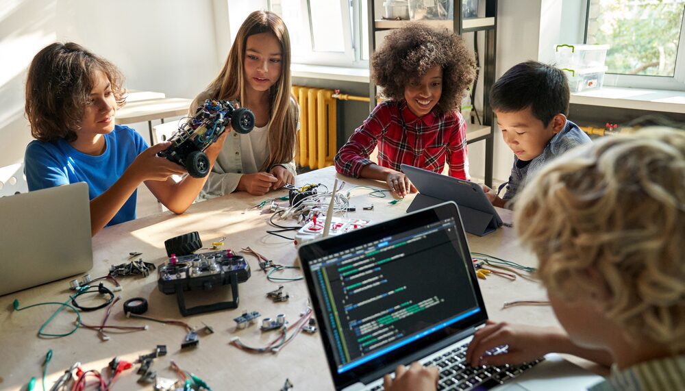 A group of kids sitting around a table with laptops.