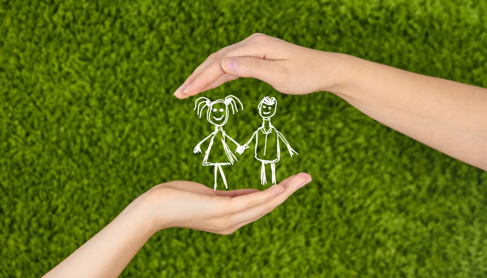 Two hands holding a drawing of a boy and girl.